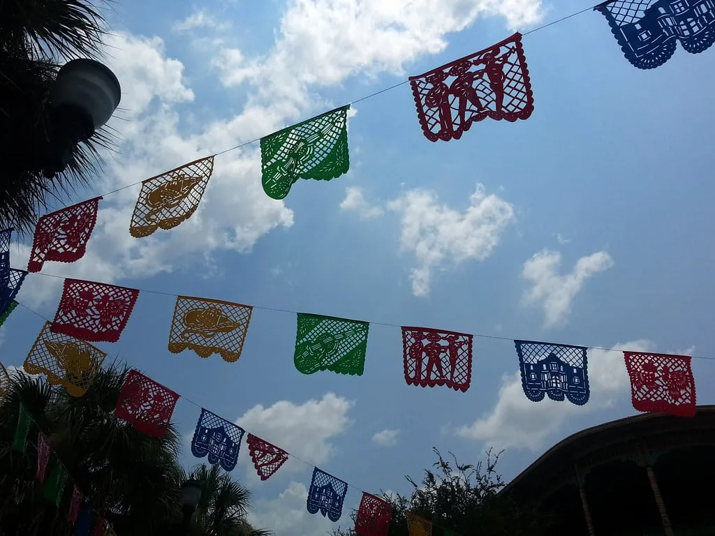 Papel picado strung over a street. The cut-paper banners are the month's most familiar image, and the one most likely to become the whole unit if nobody sets a language rule first.